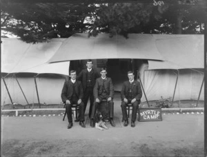 Group of unidentified young men outside a large tent, sign reads 'Myrtle Camp', includes a dog in front, [New Brighton, Christchurch?]
