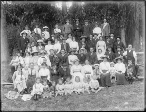 A large group of unidentified men, women and children, near a stand of eucalyptus trees, probably Christchurch district