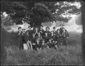 Group of young men, members unidentified, in an outdoor location with long grass and a pine tree, possibly Christchurch district