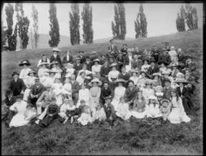Large group of unidentified men, women and children, sitting outside on a grassy slope, probably Christchurch district