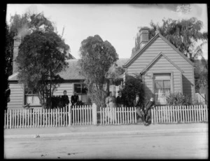 A single-storied wooden house with brick chimneys and a shingled roof, including a man, women and two boys standing in front of property, possibly Christchurch district