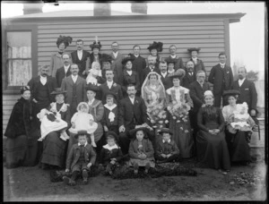 Unidentified large wedding group, showing bride and groom, wedding party and family members outside a wooden house, probably Christchurch district