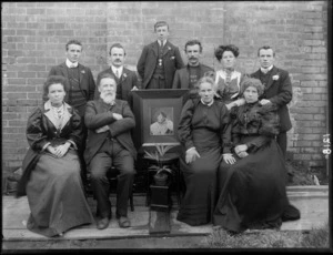 Family group, showing unidentified men and women with a framed photograph of an absent member, possibly Christchurch district