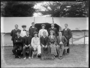 Group of unidentified men and women, with dog, outside a tent, with a sign reading 'Imperial Camp', location unidentified
