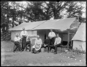 Raukura camp, showing a group of unidentified men and boys sitting outside a tent, splitting kindling, peeling potatoes, and drying dishes, location unidentified, possibly Christchurch district