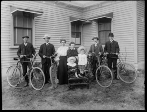 Unidentified [family?] group, shows men wearing hats with their bicycles and two small children on a chair with two women standing behind, probably Christchurch district