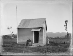 Unidentified young man sitting outside a small hut, probably Christchurch district