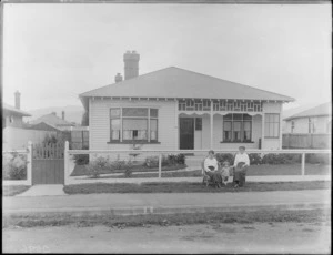 Exterior view of a single storied house, shows two unidentified women and a small child sitting on grass verge, probably Christchurch district