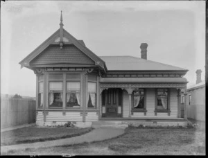 Exterior view of a single storied house, with venetian blinds and lace curtains in the window, probably Christchurch district