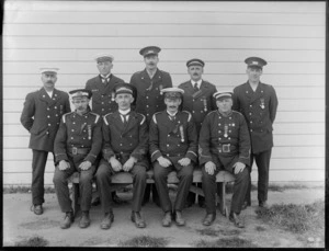 Group of nine unidentified firemen in uniform from the Christchurch Fire Brigade, some wearing a badge on cap, reading 'NZRFB Addington', Christchurch