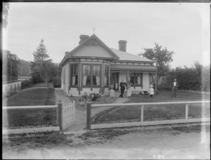 Exterior view of a single storied house, shows two unidentified men and a young girl with a pram, probably Christchurch district