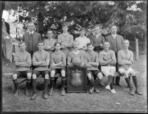 Unidentified group portrait of mixed mens and boys [college?] football team in uniforms and coaches, with shield trophy and soccer ball, probably Christchurch region