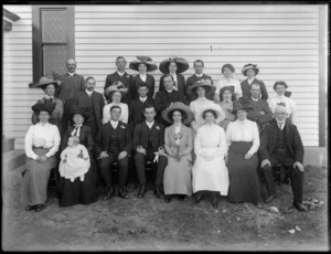 Wedding group portrait, unidentified bride and groom with extended family and priest, in front of wooden building outside wall, probably Christchurch region