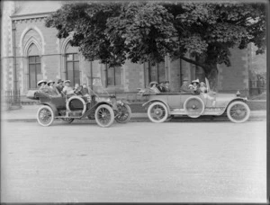 Two touring cars carrying unidentified adults and children in hats, one with chauffeur, parked outside Canterbury Museum, Christchurch