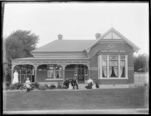 Brick house with veranda, man [J Pycroft?] (plaque on house), two women and girl with bicycle, in front, probably Christchurch region