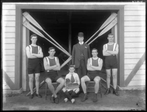 Unidentified men's coxed four rowing team with a young boy coxswain and coach, with crossed oars behind, outside the Avon Rowing Club boatshed, Christchurch