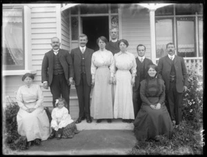 Group portrait of unidentified people, including a priest and young girl, outside the entrance of a house, probably Christchurch region