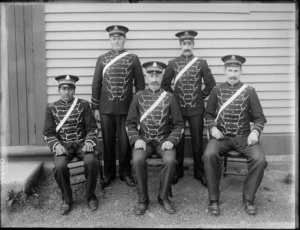 Group portrait of five unidentified male members of The Salvation Army in ornate uniforms, hats and sashes, in front of a wooden building, probaly Christchurch region