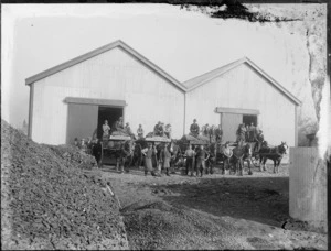 New Zealand State Coal Depot building, showing unidentified workmen with loaded sacks of coal on Clydesdale drawn wagons, in front of a large warehouse with open doors, probably Christchurch region
