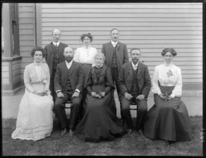 Family portrait, unidentified elderly couple with adult family members, three men and three women, in front of a wooden house, women holding leaves, probably Christchurch region