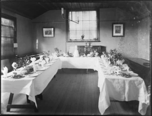 Small wedding reception room with trestle tables, three tiered wedding cake, plates and wine ready for guests, probably Christchurch district