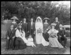 Wedding party portrait, unidentified bride in long veil and groom with bridesmaids, groomsmen and young flower girl and parents, pine trees beyond, probably Christchurch region