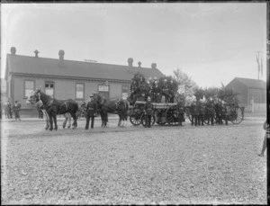 Christchurch Railways Volunteer Fire Brigade [float?], unidentified men in uniforms, medals and hats, with horse drawn wagons carrying fire fighting equipment decorated in foliage, Railways depot behind