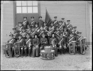 Group portrait of Salvation Army Brass Band, unidentified men and two women with their instruments and in ornate uniforms and hats and flag, probably Christchurch region