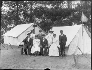 Group of unidentified adults in front of two tents with a [New Zealand?] flag and 'Ivy Camp' sign on one, and an American flag on the other, [Sumner?], Christchurch
