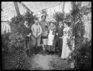 Group of unidentified people in costumes, as noblemen and gamekeeper with guns, a farmer with turnip, milkmaid with pail, and a dandy and his wife, in a greenhouse, probably Christchurch region