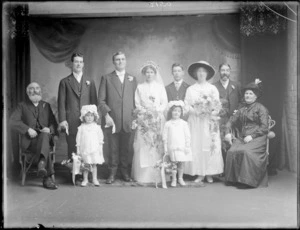 Studio wedding party portrait, unidentified bride with long veil and groom, family members, bridesmaid, best man and two young flower girls with bonnets, Christchurch