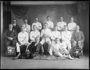 Studio portrait of unidentified men's cricket team, with players in white uniforms, with bat and two shield trophies, Christchurch