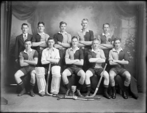 Studio portrait of unidentified men's hockey team members in uniforms and coach, with hockey sticks, goal keeper in pads, hockey ball and trophy cup, Christchurch