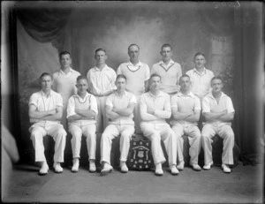 Studio portrait of men's cricket team, unidentified players dressed in white uniforms, with shield trophy, Christchurch