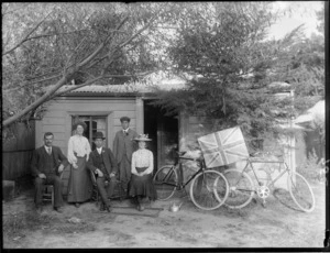 Group of unidentified people outside a house, probably Christchurch district, includes two bicycles and a British flag