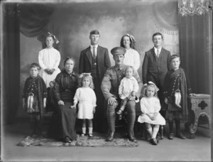 Studio portrait of unidentified family group, showing a man in military uniform, his wife and nine children, including two boys in Scottish national costume, probably Christchurch district
