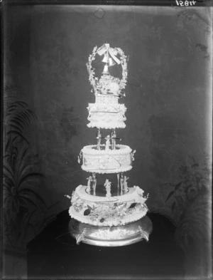 Three-tier wedding cake, with little angel figurines and three bells tied to ribbon at the top