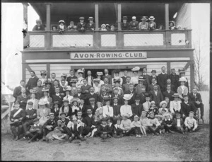 Avon Rowing Club building, with unidentified men and women club members with children on balcony and on grass slope in front, wearing an assortment of hat and caps, some men in uniforms, boy with dog, Christchurch