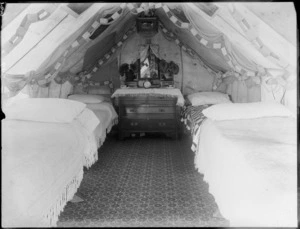 Interior of a tent, which has been decorated with paper streamers, and contains four beds and a dressing table, possibly Christchurch district