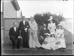 Wedding group, including bride and groom, bridesmaids, flowergirls, and two other unidentified men, in front of a garden trellis, possibly Christchurch district
