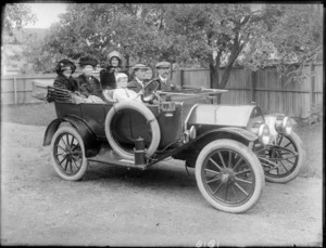 A motorcar, with three female passengers in the back, two men in the front, and a boy at the wheel, all unidentified, in a driveway, possibly Christchurch district