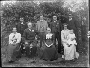Family group, showing unidentified men and women, one holding a baby, all without hats, in a garden, possibly Christchurch district