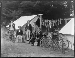 Rabbit-hunting party, showing six men, with bicycles, guns, and dogs, including dead rabbits strung between two tents behind, possibly Christchurch district