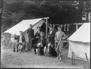 Rabbit-shooting party, showing six men with guns and dogs, standing beside two tents, which have a row of dead rabbits strung between them, possibly Christchurch district