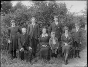 Family group portrait in the backyard, unidentified older parents with their two daughters and four sons, bushes behind, probably Christchurch region