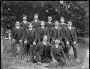 Group of unidentified men wearing business attire, with a coiled rope placed on ground in front, in an outdoor location, possibly Christchurch district