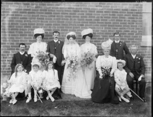 Wedding party portrait, unidentified bride and groom with their parents, bridesmaid and best man and flower girls, page boys with small crooks and hats, outside a brick walled building, probably Christchurch region