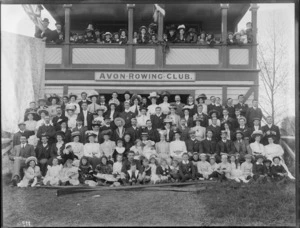 Avon Rowing Club building, with unidentified club members and children on balcony with British flag, and on grass slope in front with oars, wearing an assortment of hat and caps, Christchurch