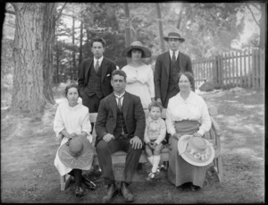 Family group, showing unidentified men, women and children, on a park bench, in an outdoor location, possibly Christchurch district