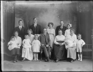 Studio portrait of a family group, showing unidentified men, women and children, with a painted backdrop